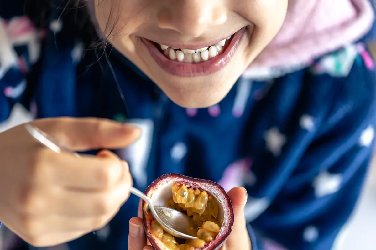 Niña comiendo fruta ácida — alimentos que pueden manchar y dañar los dientes